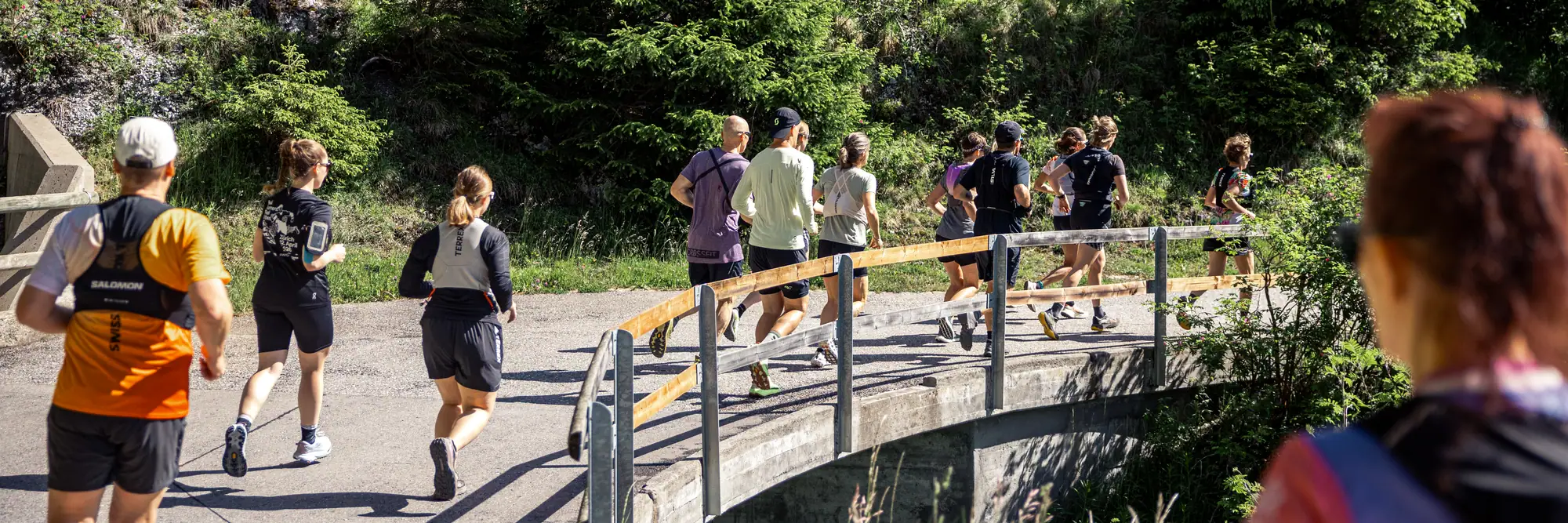 A training group running over a small road bridge in the forest.