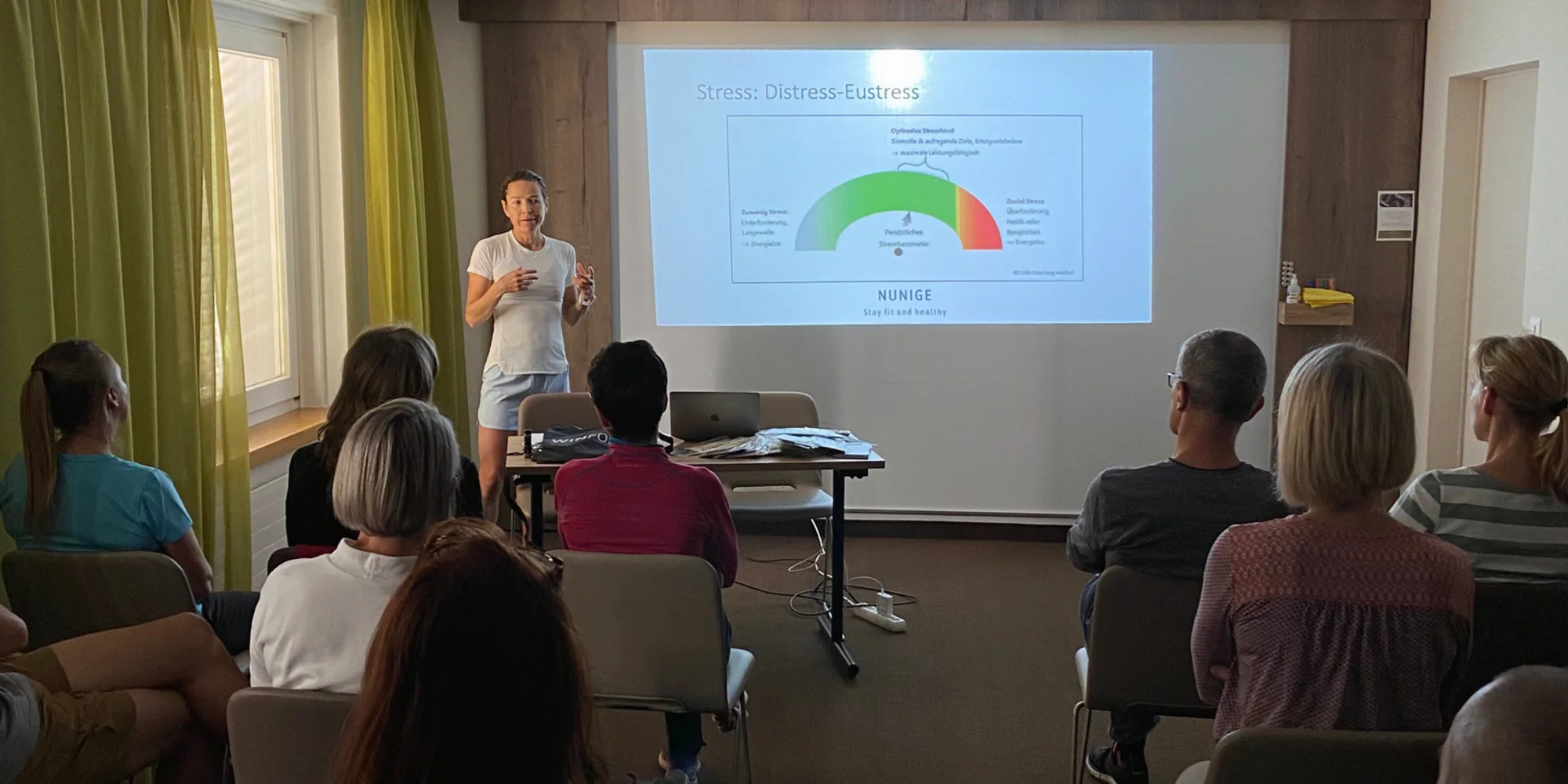 Eine Referentin erklärt einer sitzenden Gruppe eine projizierte Folie zu Distress und Eustress.