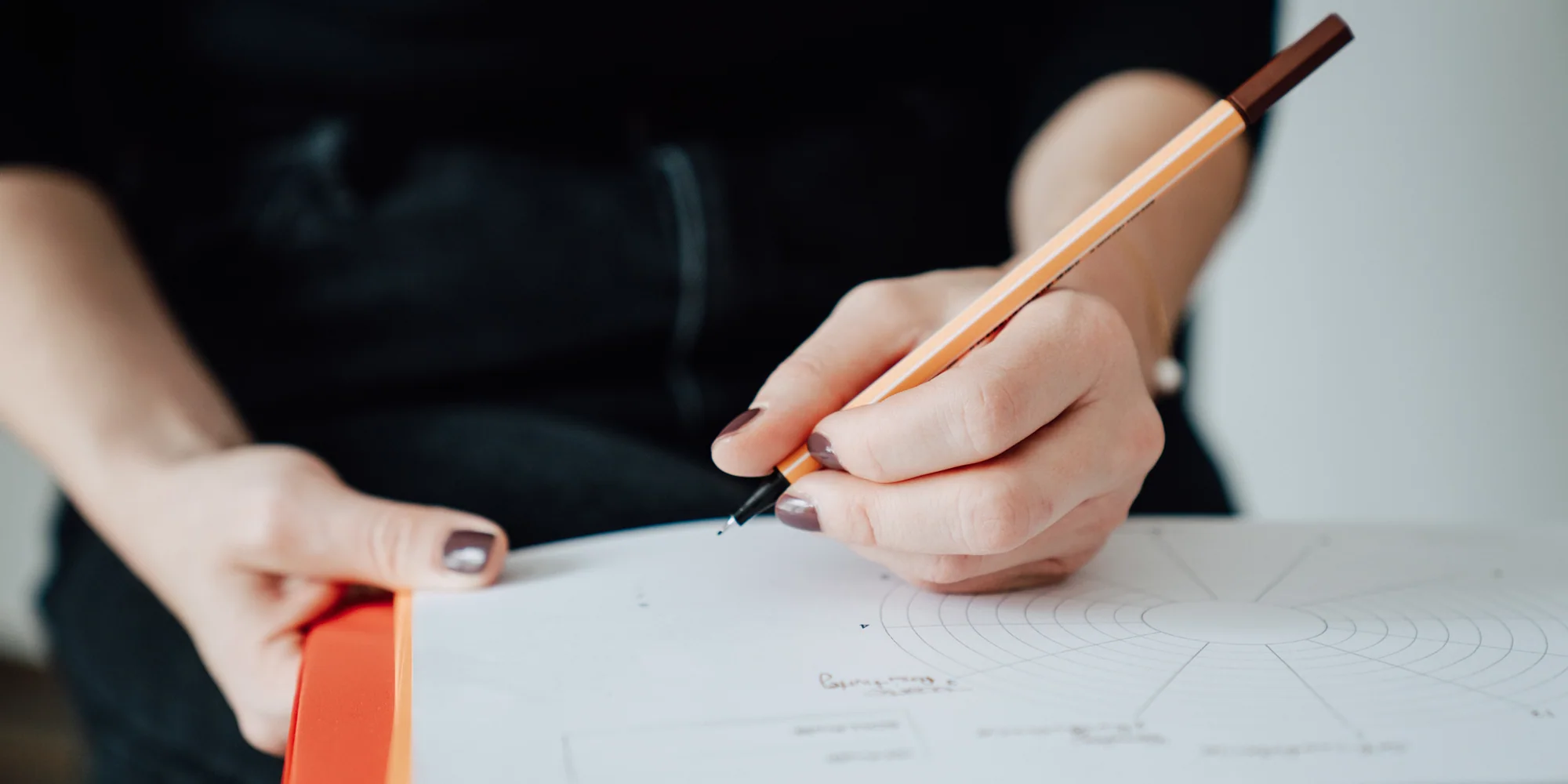 Nahaufnahme zweier Hände, eine setzt mit einem orangen Stift einen Punkt in ein kreisförmiges Diagramm auf Papier.