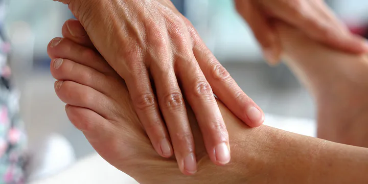 Two hands working on the foot of a person lying down, fingers across the instep.